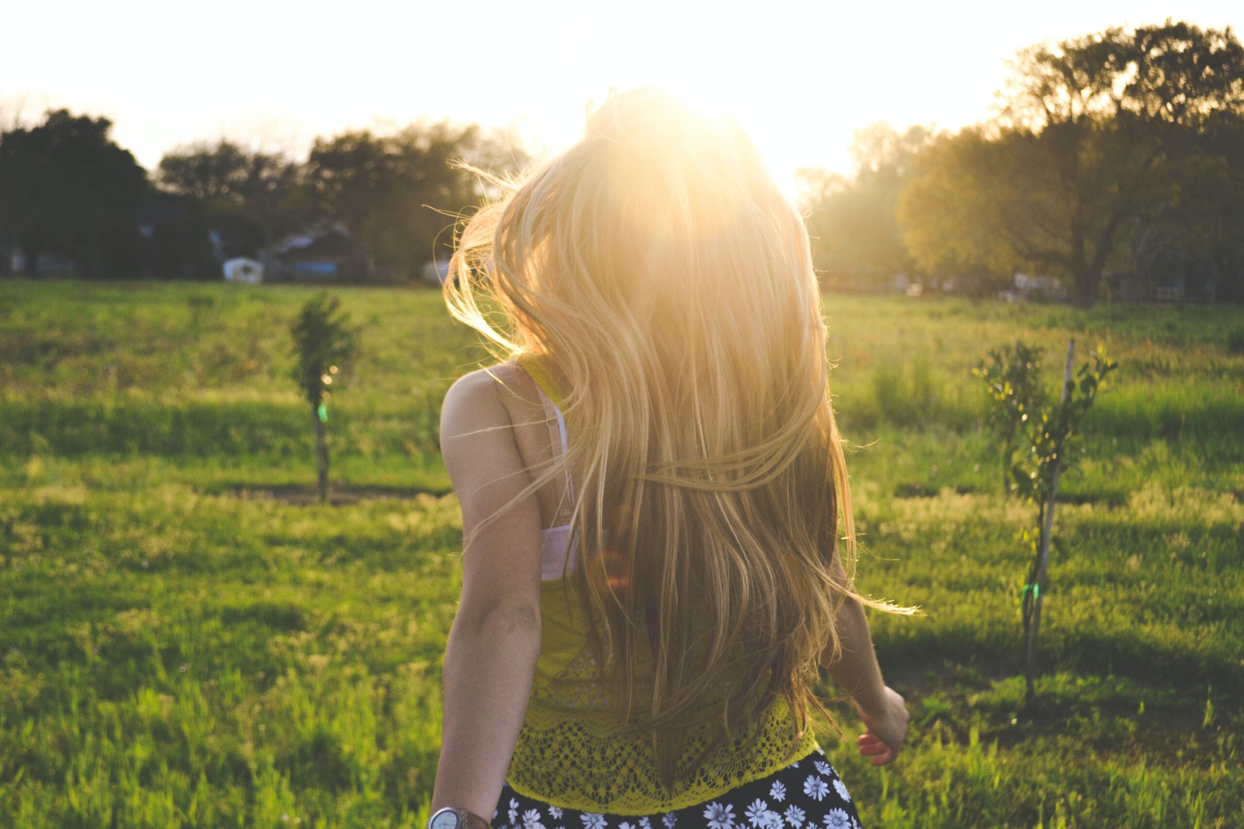 girl happily running towards sunset in green grass